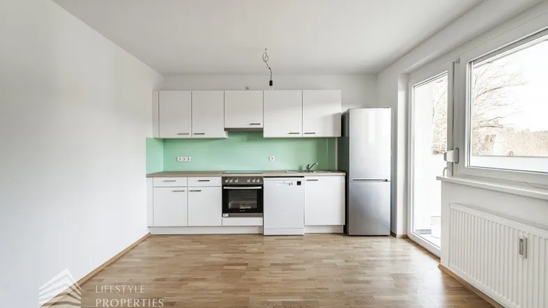 Helle, moderne Küche mit weißen Schränken, grüner Rückwand und Holzboden.