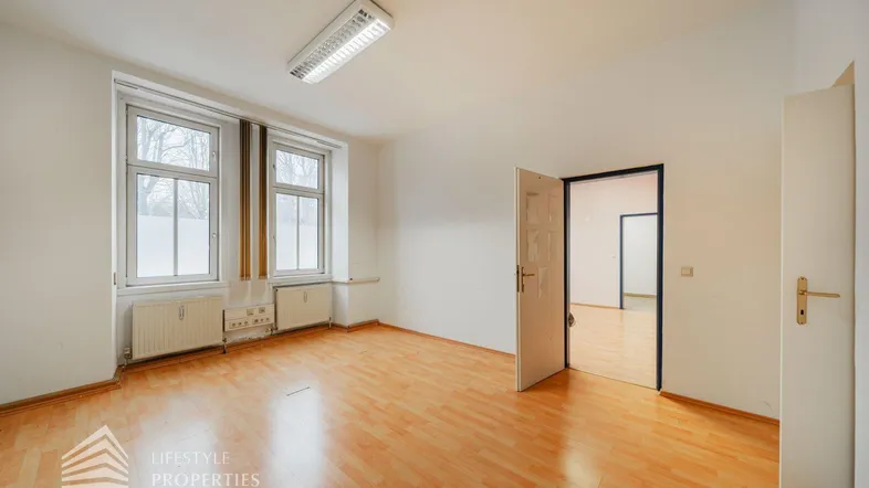 Helles Büro mit Holzboden, zwei großen Fenstern und weiß gestrichenen Wänden, bereit zur Einrichtung.