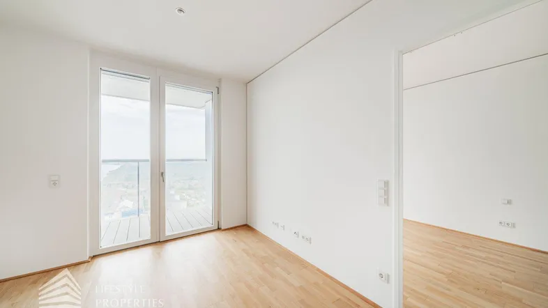 Helles Zimmer mit Holzboden und Zugang zu einem Balkon, bietet einen weiten Ausblick.