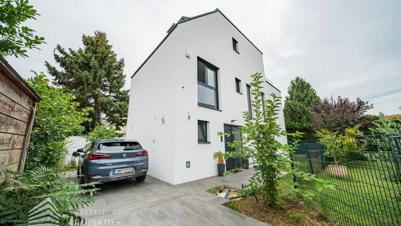Modernes Einfamilienhaus mit weißer Fassade, Vorgarten und Stellplatz für ein Fahrzeug.