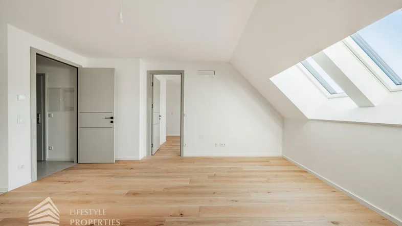 Heller Raum im Dachgeschoss mit Holzboden, weißen Wänden und großen Dachfenstern.