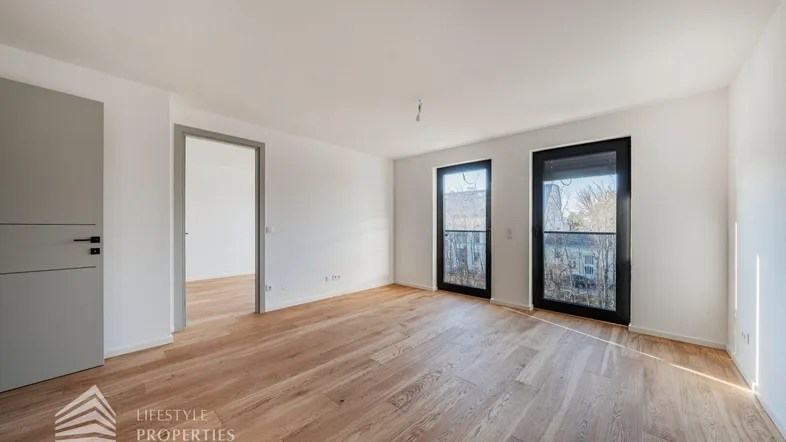 Helles Zimmer mit neuem Parkettboden und großen Fenstern, die viel Tageslicht hereinlassen.