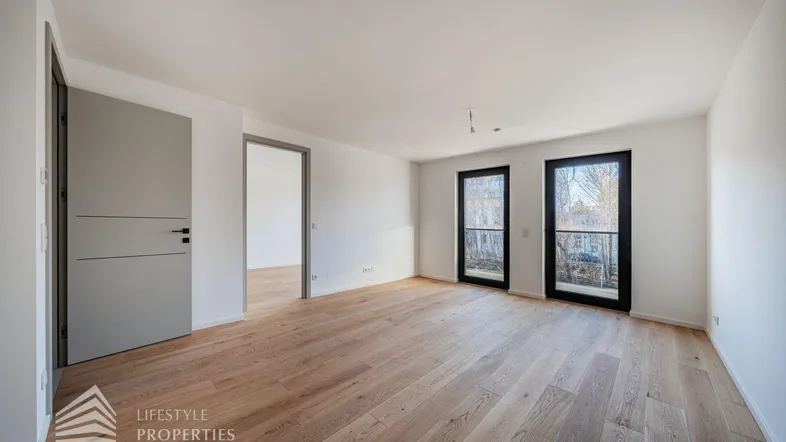 Helles Zimmer mit Holzboden und zwei Fenstertüren, die zu einem französischen Balkon führen.