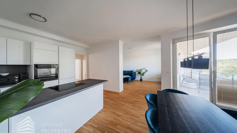 Moderner offener Wohn-Essbereich mit integrierter Küche, Holzboden und Zugang zum Balkon.