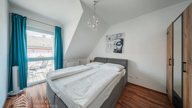 Helles Schlafzimmer mit Holzboden, Dachschräge und Zugang zu einem kleinen Balkon.