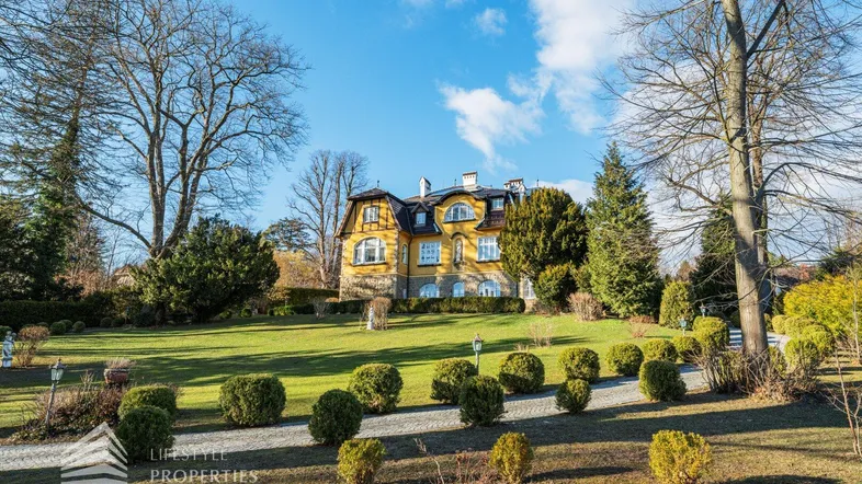 Elegante Stadtvilla mit weitläufigem, gepflegtem Garten und altem Baumbestand unter blauem Himmel.