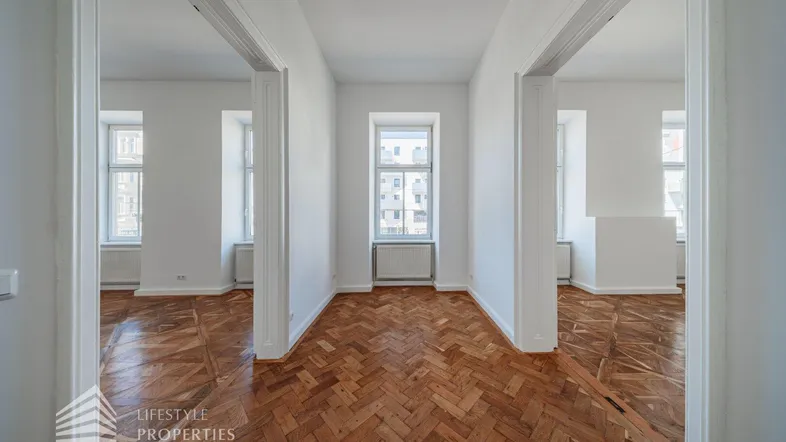 Heller Innenraum mit Fischgrätparkett und hohen Türen, der mehrere Zimmer verbindet.