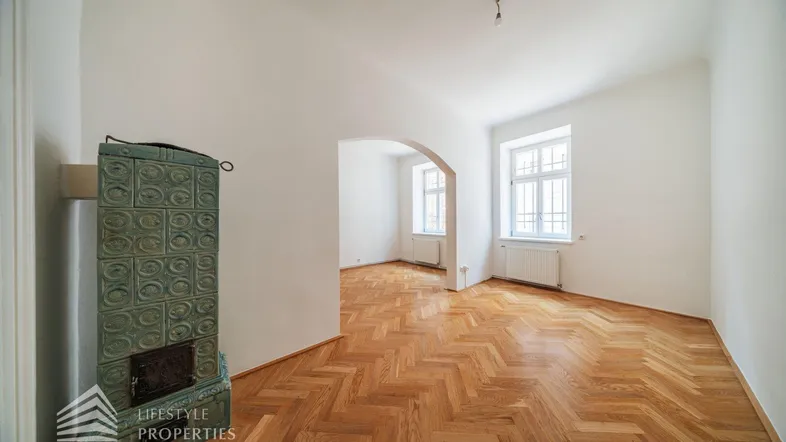 Helles Wohnzimmer mit Fischgrätparkett und einem traditionellen Kachelofen, bereit zur individuellen Gestaltung.