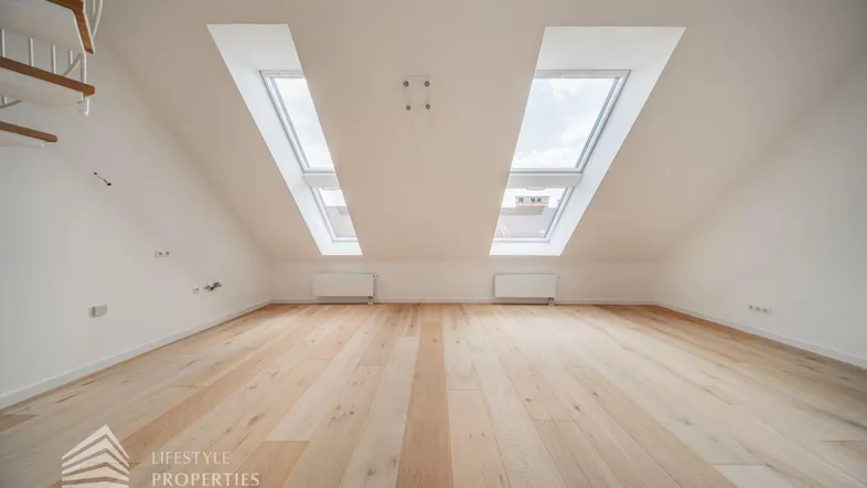 Heller Dachgeschossraum mit schrägen Wänden, zwei großen Dachfenstern und elegantem Holzfußboden.