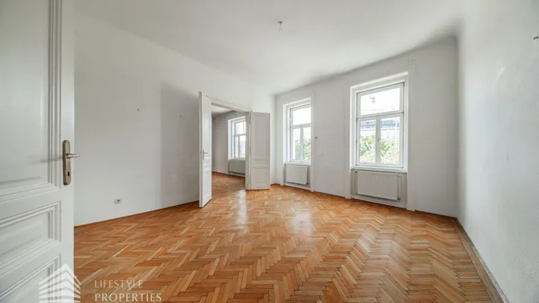 Helles, leeres Zimmer mit Fischgrätparkett und hohen Fenstern, bereit zur individuellen Gestaltung.