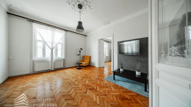Helles Wohnzimmer mit Fischgrätparkett, Stuckdecke und modernem TV-Bereich an der Wand.