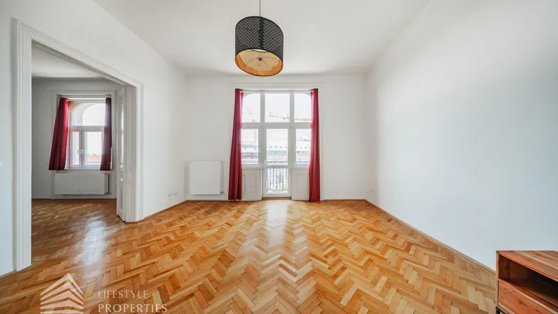 Helles Wohnzimmer mit Fischgrätparkett, hohen Decken und Zugang zum Balkon.