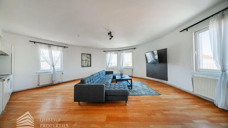 Helles und geräumiges Wohn-Esszimmer mit Holzboden, bequemer Couch und integrierter Küchenzeile.