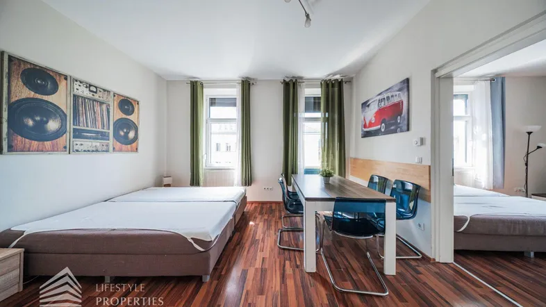 Helles Zimmer mit zwei Betten, Esstisch und Holzboden, ideal für Wohnen und Schlafen.