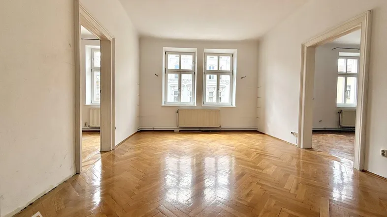 Helles Zimmer mit Fischgrätparkett, weißen Wänden und zwei Fenstern, bereit zur individuellen Gestaltung.