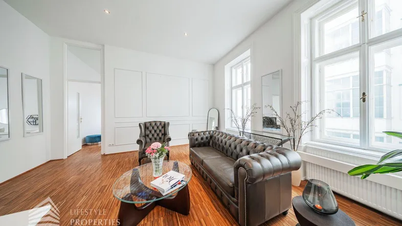 Geräumiges Wohnzimmer mit elegantem Ledersofa, Holzboden und großen Fenstern, die viel Tageslicht hereinlassen.