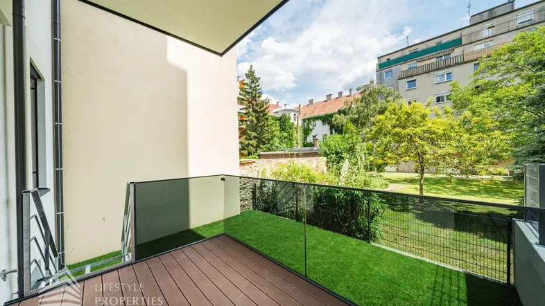 Moderner Balkon mit Holzboden und Glasgeländer, bietet Blick auf den begrünten Innenhof.