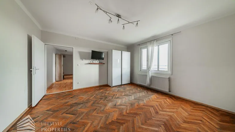 Geräumiges Zimmer mit Fischgrätparkett, weißen Wänden und Fenster mit Ausblick.