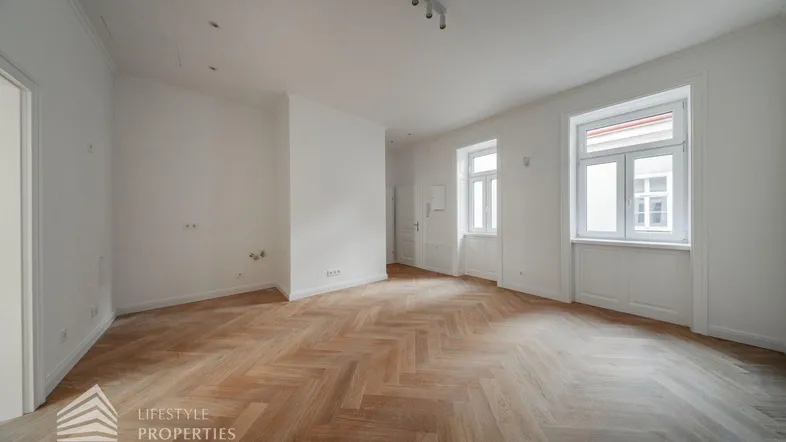 Helles Zimmer mit Fischgrätparkett und hohen Fenstern, bereit zur individuellen Gestaltung.