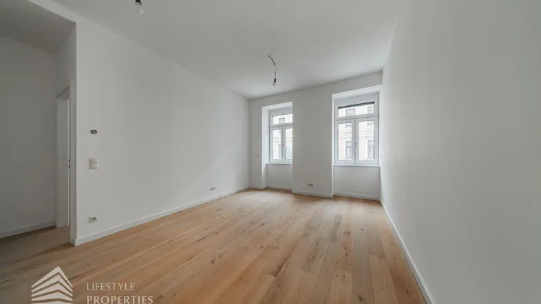 Helles, leeres Wohnzimmer mit neuem Holzboden und zwei großen Fenstern, bereit zur Gestaltung.