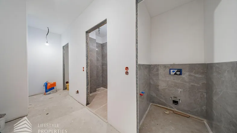 Unfertiger Innenraum mit gefliestem Bereich für ein zukünftiges Badezimmer oder einen Hauswirtschaftsraum.