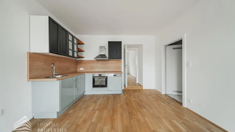 Moderne Einbauküche mit hellen Holzdetails und dunklen Oberschränken in einem offenen Wohnbereich.