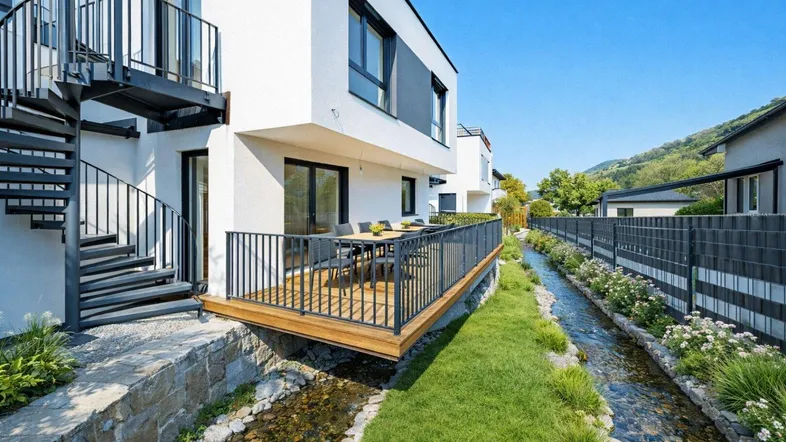 Moderne Terrasse mit Holzboden und Esstisch, direkt an einem kleinen Bachlauf gelegen.