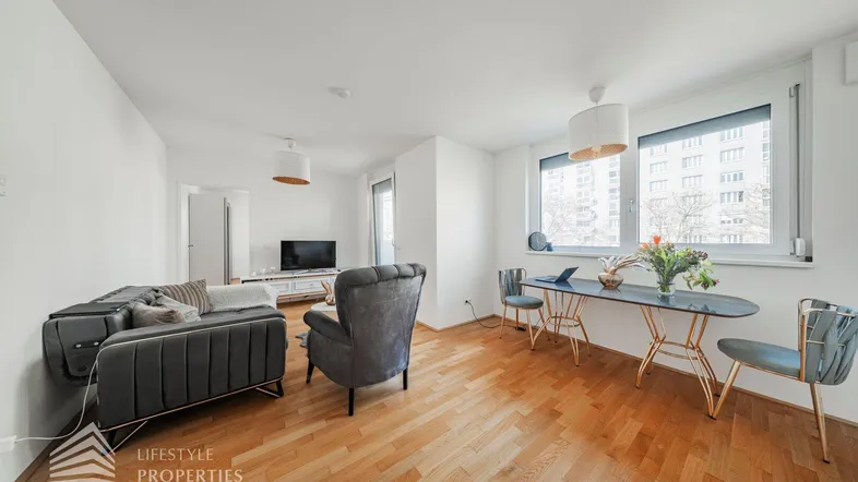 Helles Wohnzimmer mit Parkettboden, bequemen Sofas und einem modernen Schreibtischbereich am Fenster.