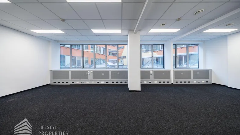 Geräumiges, leeres Büro mit großen Fenstern, die viel Tageslicht hereinlassen und einen Blick auf den Innenhof bieten.