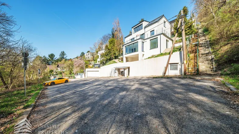 Moderne Villa am Hang mit großen Fenstern, Zufahrt und umgebender Natur.