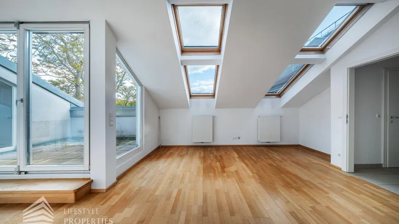 Heller Dachgeschossraum mit Parkettboden, großen Dachfenstern und direktem Zugang zur Terrasse.