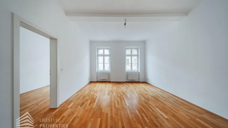 Helles, leeres Zimmer mit Parkettboden und zwei Fenstern, bereit zur individuellen Gestaltung.