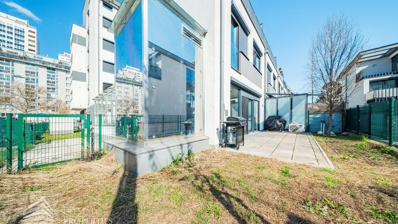 Moderne Gebäudefassade mit einer gepflasterten Terrasse und einem kleinen Gartenbereich im Freien.