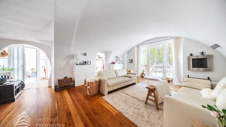 Helles Wohnzimmer mit gewölbter Decke, Holzboden und Zugang zu einem Außenbereich.