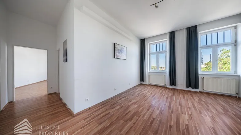 Helles, leeres Zimmer mit Parkettboden und zwei großen Fenstern, bereit zur individuellen Gestaltung.