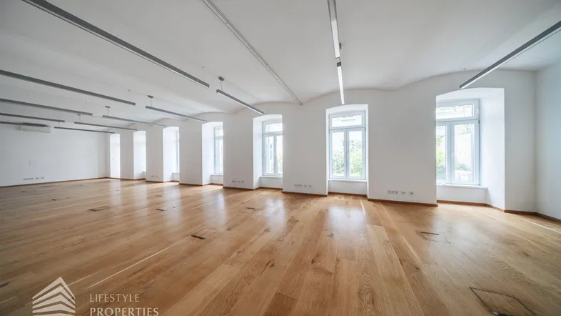 Großer, heller Raum mit Holzboden, hohen Decken und vielen Fenstern, ideal für Büronutzung.