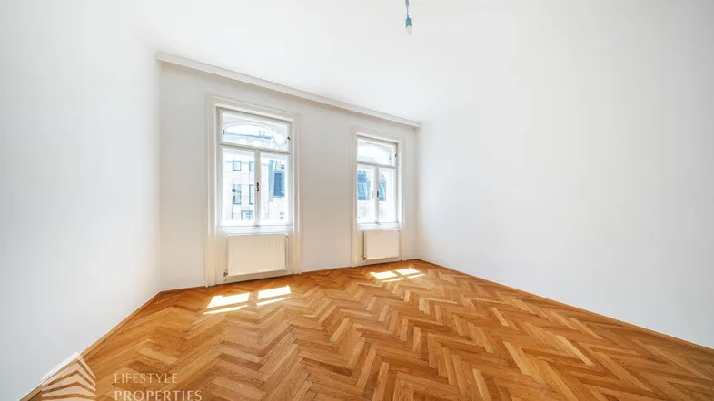 Helles Zimmer mit Fischgrätparkett und zwei großen Fenstern, ideal als Wohn- oder Schlafzimmer.