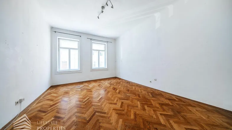 Helles Zimmer mit Fischgrätparkett und zwei Fenstern, ideal als Wohn- oder Schlafzimmer.
