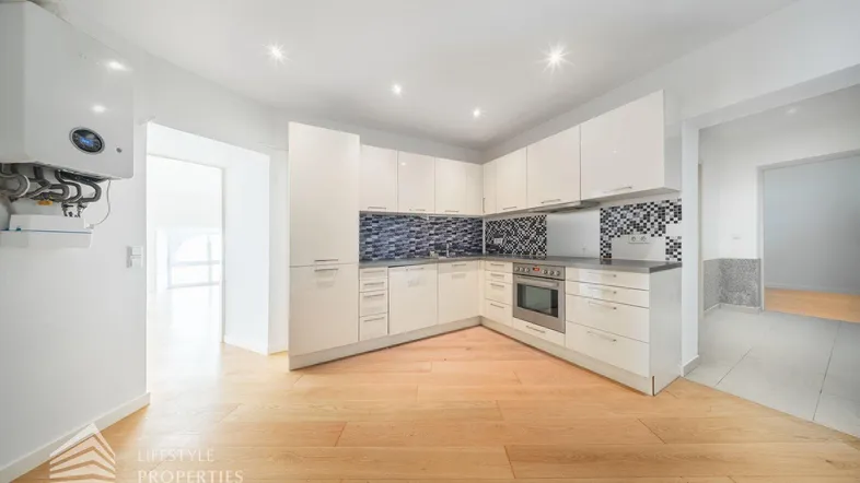 Moderne Einbauküche mit weißen Hochglanzfronten, dunkler Arbeitsplatte und blauen Mosaikfliesen.