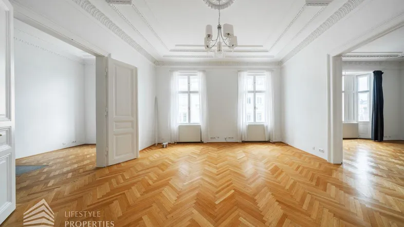 Großzügiger Raum mit Fischgrätparkett, hohen Decken und eleganten Stuckverzierungen, ideal als Wohnzimmer.