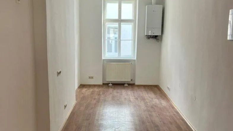 Leerer Raum mit Laminatboden, Fenster und Gastherme, bereit für die individuelle Gestaltung.