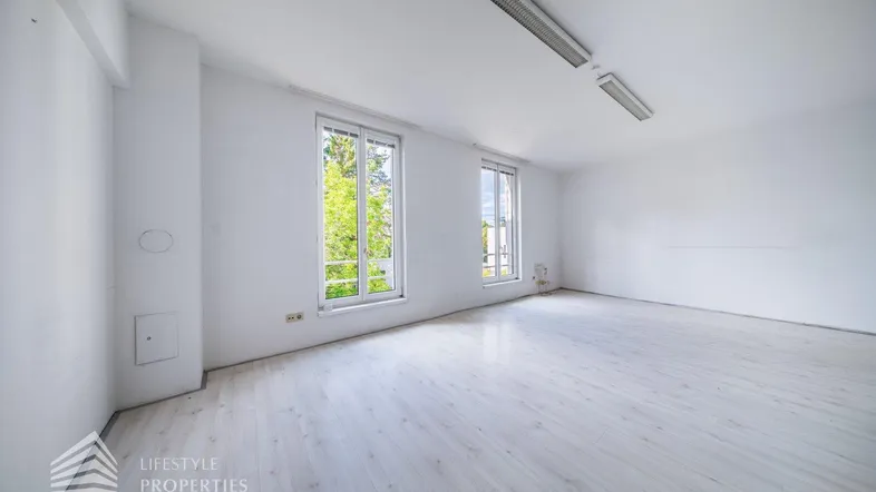 Helles, leeres Zimmer mit großen Fenstern und hellem Laminatboden, bereit zur individuellen Gestaltung.