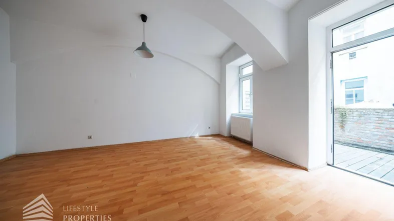 Helles, leeres Zimmer mit Holzboden, gewölbter Decke und Zugang zu einem Außenbereich.