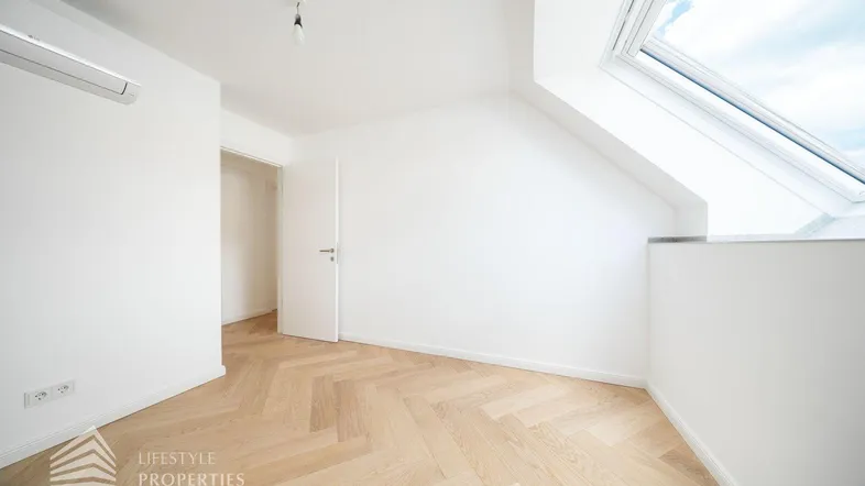 Helles Dachzimmer mit modernem Fischgrätparkett, Dachfenster und Klimaanlage.