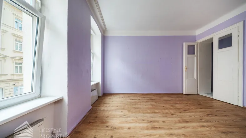 Geräumiges Zimmer mit lila Wänden, Holzboden und großen Fenstern, die viel Tageslicht hereinlassen.