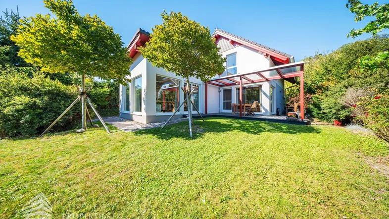 Modernes Einfamilienhaus mit großem Garten und überdachter Terrasse unter blauem Himmel.