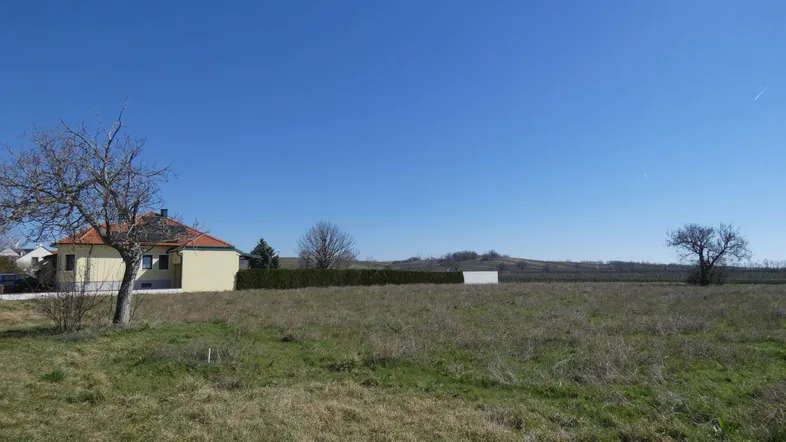 Weitläufiges Grundstück mit Blick auf ein Einfamilienhaus und die umliegende Landschaft unter blauem Himmel.