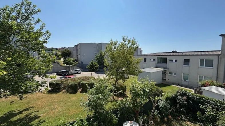 Blick von einem Balkon auf den Gemeinschaftsgarten mit Sitzgelegenheiten und umliegenden Gebäuden.