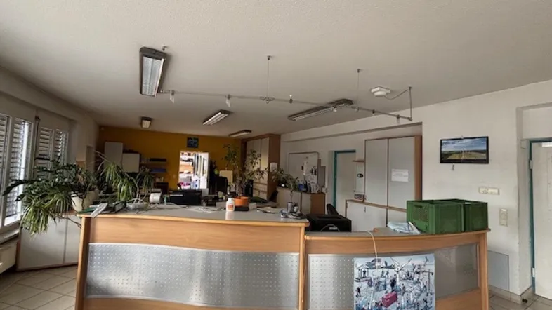 Empfangsbereich eines Büros mit Rezeptionstresen, Pflanzen und gelber Akzentwand, ausgestattet mit Fliesenboden.