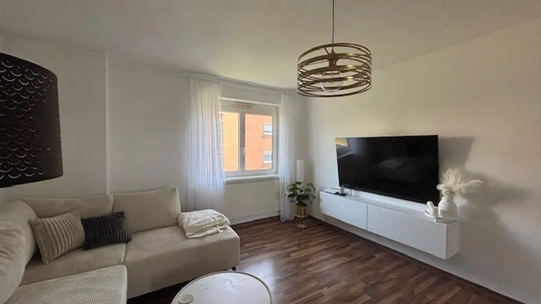 Helles Wohnzimmer mit beigem Ecksofa, Holzboden und modernem Deckenlicht.